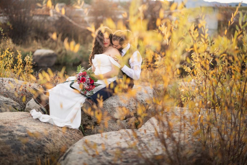 White-dressed figure seated on rocks amid golden autumn foliage holding a red bouquet.