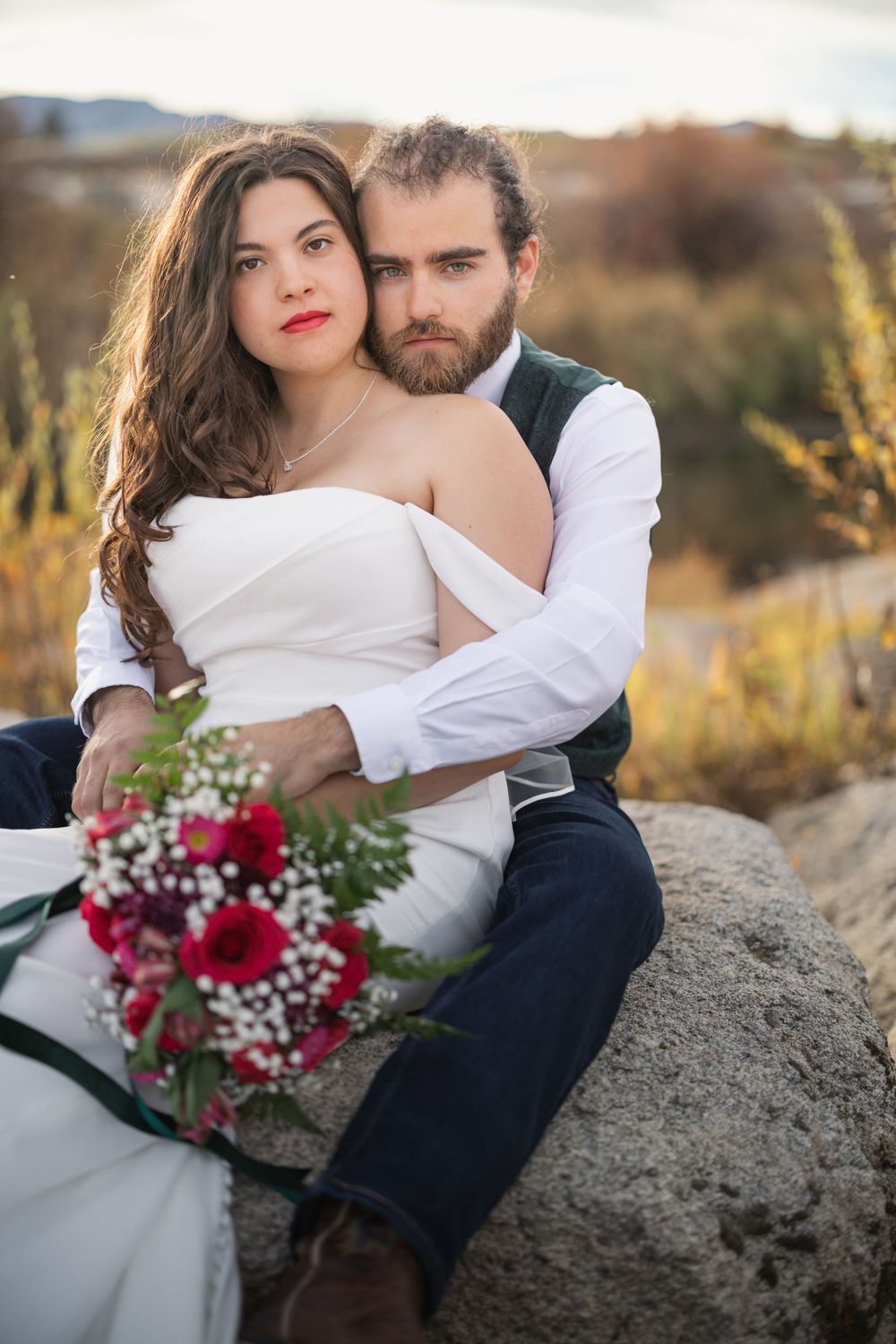 Romantic portrait on rocky terrain with autumn colors and red floral bouquet.