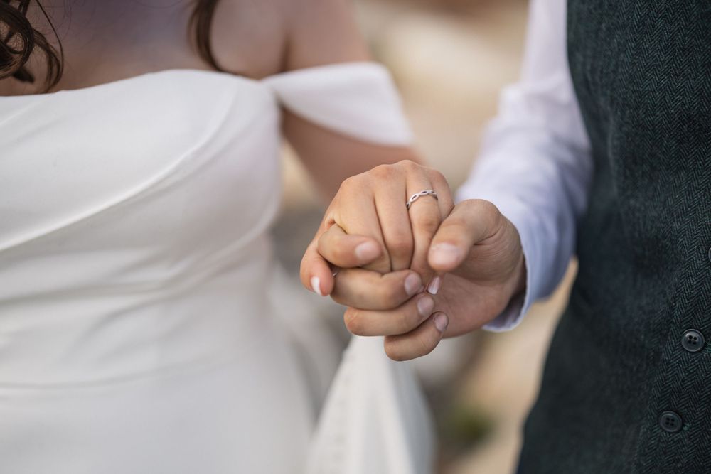 Detail shot of clasped hands showing wedding rings against formal attire.