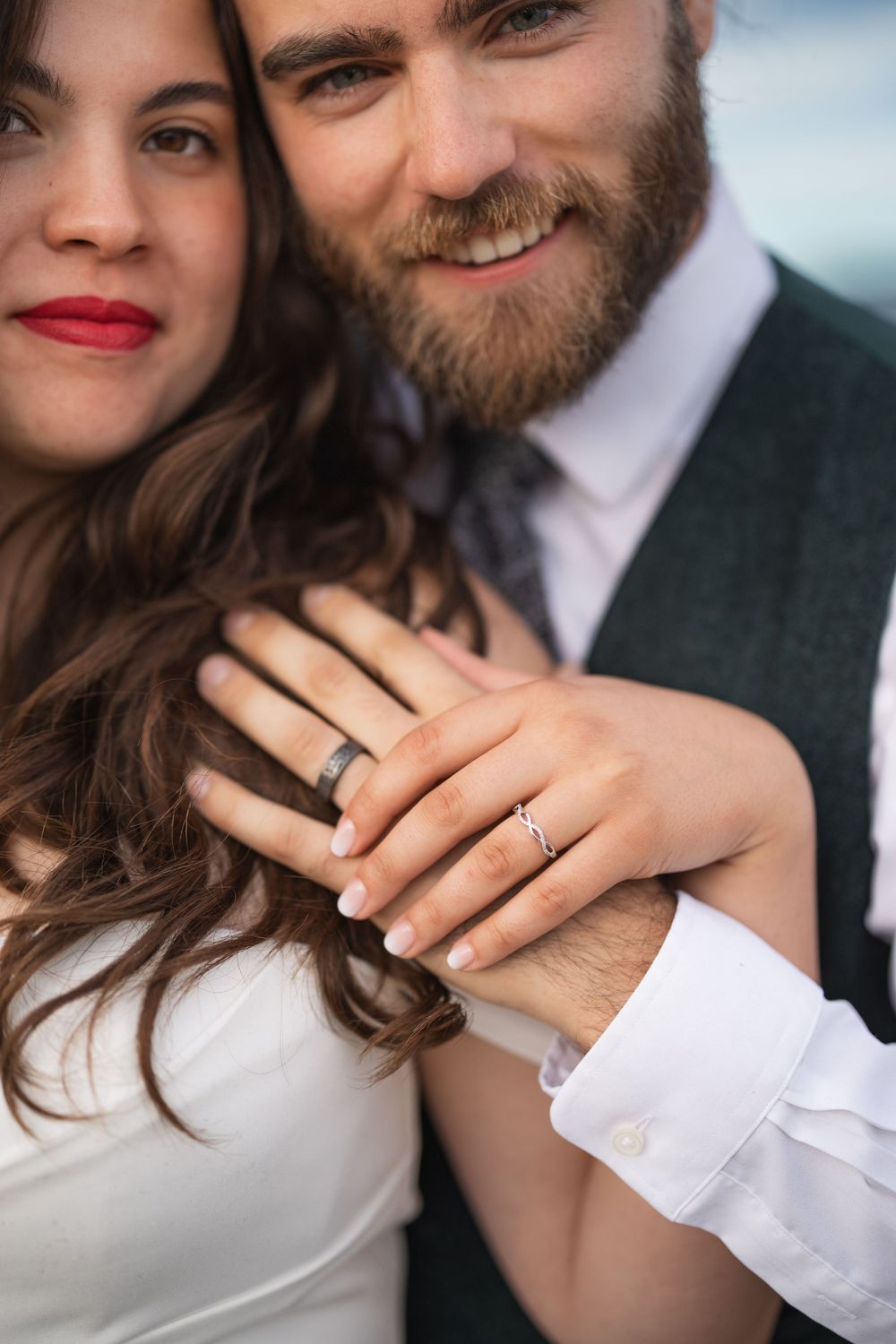 Close-up of wedding rings and hands with mountainous background.