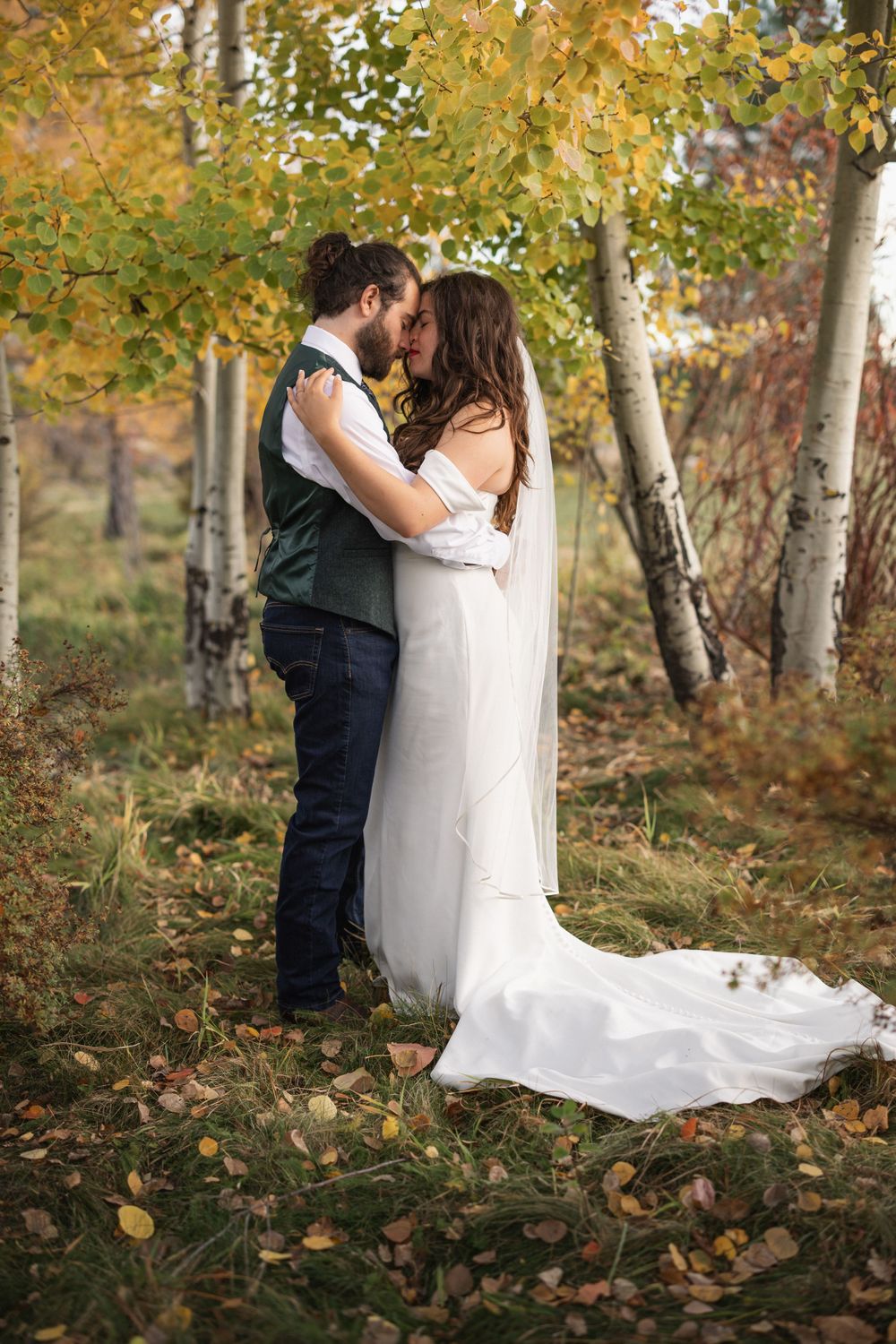 Wedding couple sharing intimate moment among autumn birch trees with fallen leaves.