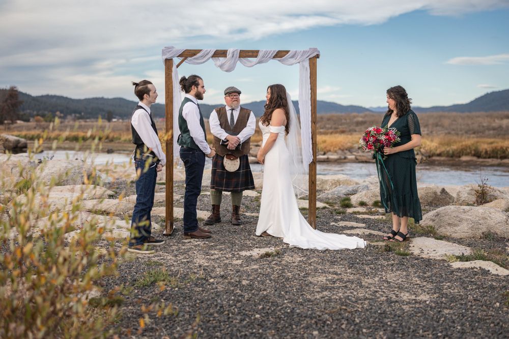 An intimate outdoor wedding ceremony under a simple arch with mountain views in the background.