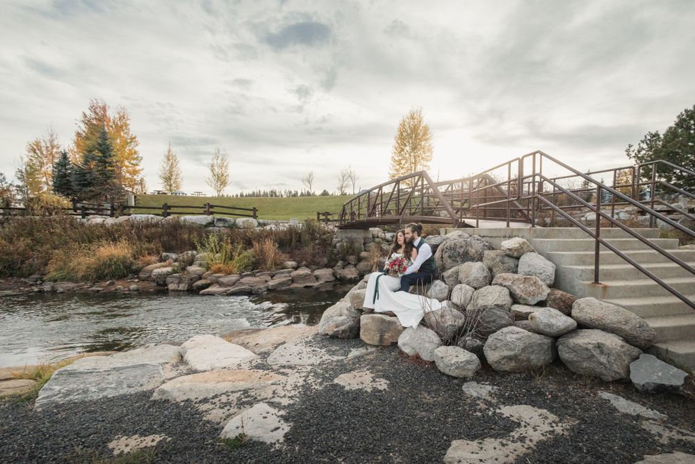 Rustic metal bridge over rocky river with autumn trees in background.