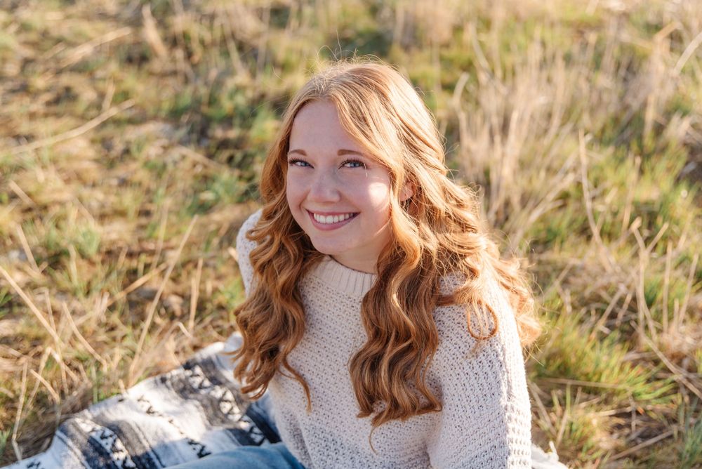 Close-up outdoor portrait wearing a cozy cream sweater against a natural landscape setting.