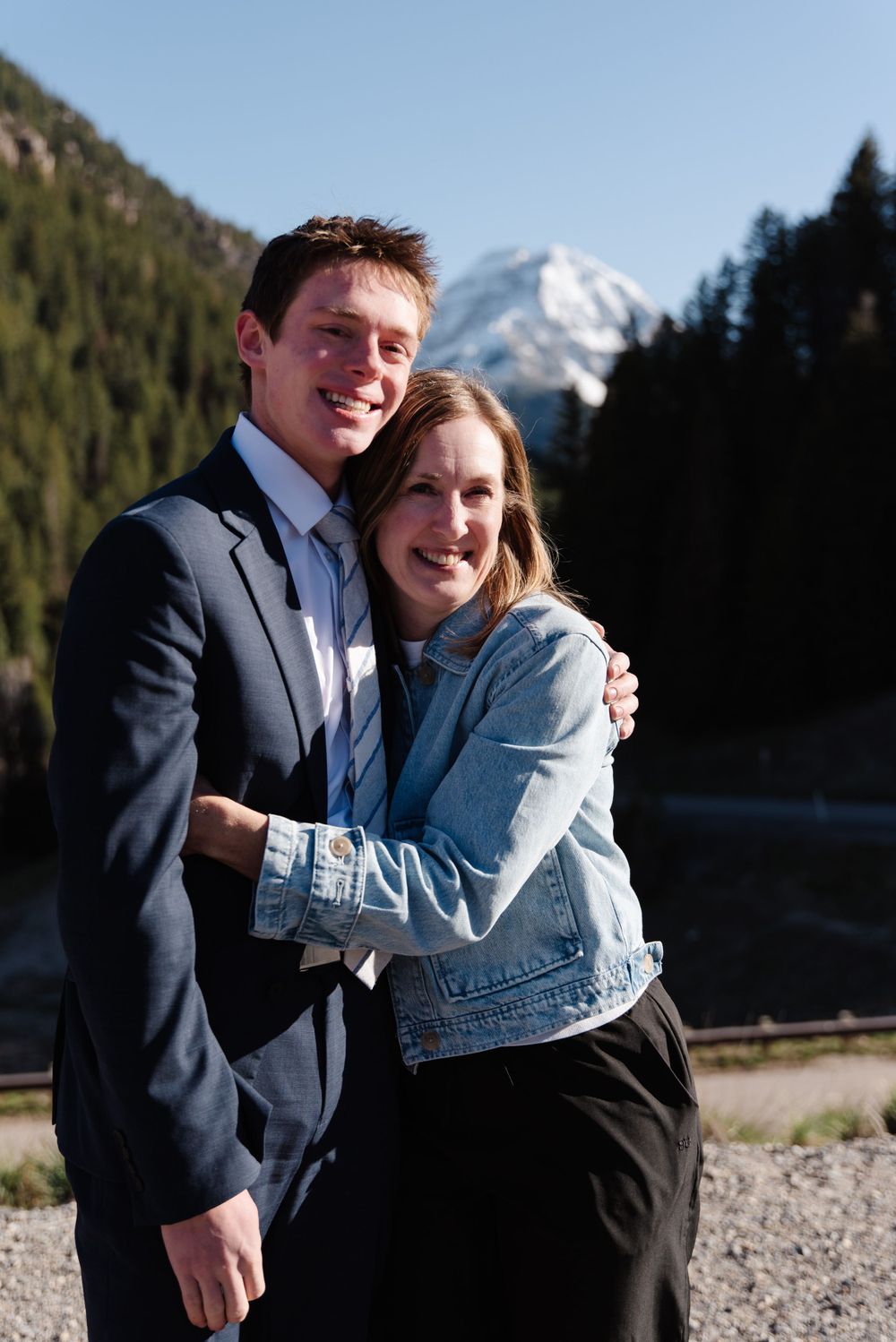 Couple embracing outdoors with snow-capped mountain peaks visible in the background.