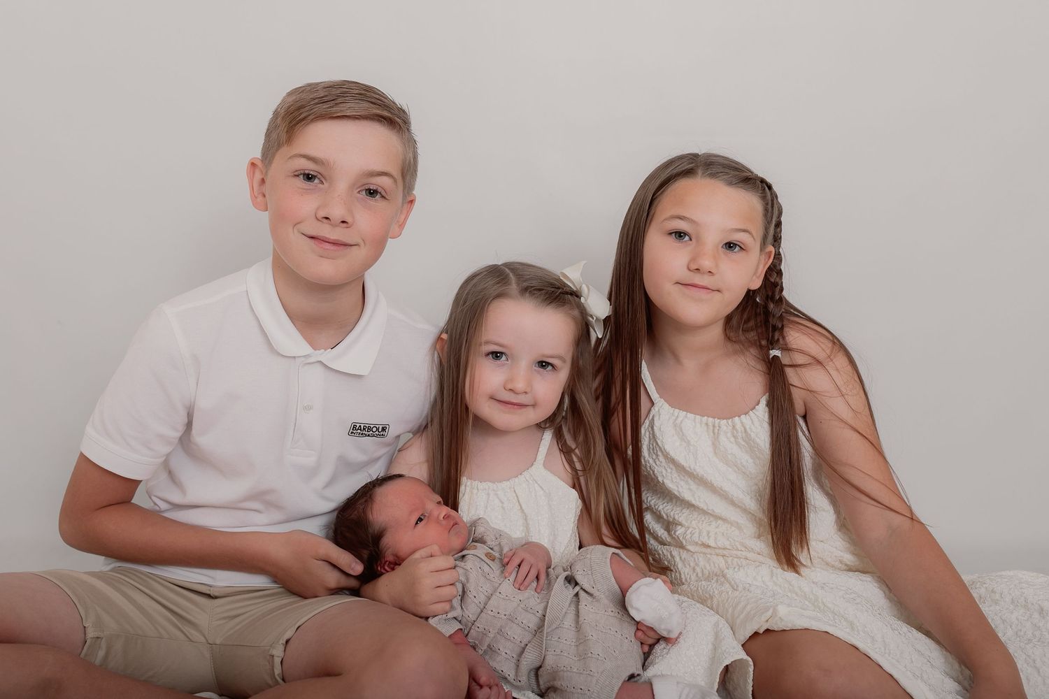 Family group photo with siblings in coordinating white outfits against grey backdrop. Photographer. Hull. East Yorkshire. Photography