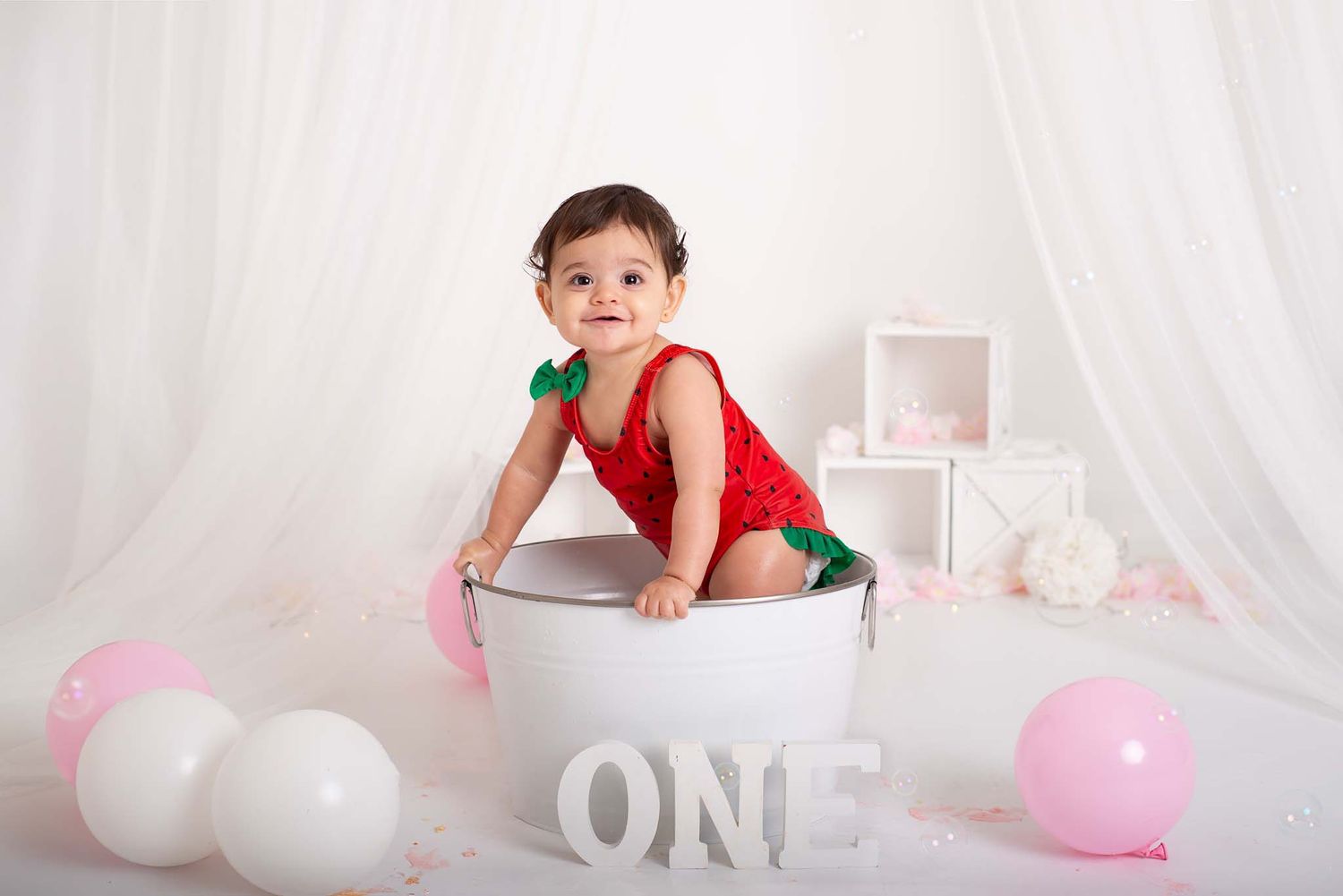 one year old in white tub with pink and white balloons for first birthday photos in studio in Baltimore Ontario Northumberland