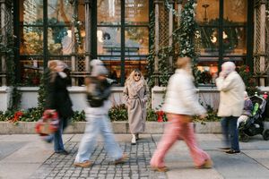 Busy city street with motion-blurred pedestrians walking past decorated storefronts.