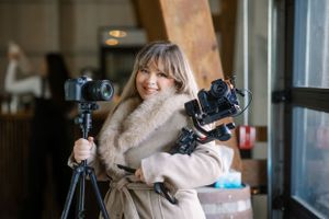 Photographer holding two professional cameras with tripod setup in cozy indoor setting with warm lighting.