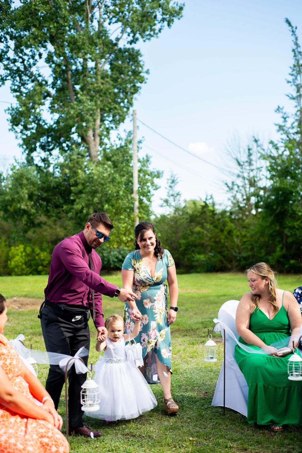 A wedding reception outdoors with guests enjoying themselves on a sunny day with green trees in the background.
