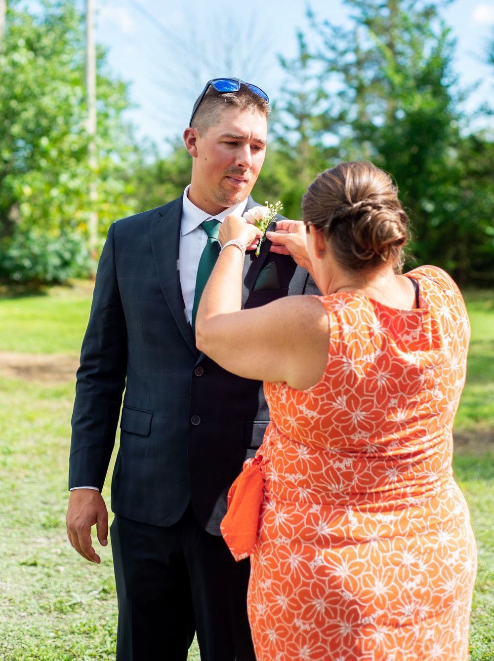 A corsage is pinned onto a suit jacket at an outdoor wedding ceremony.