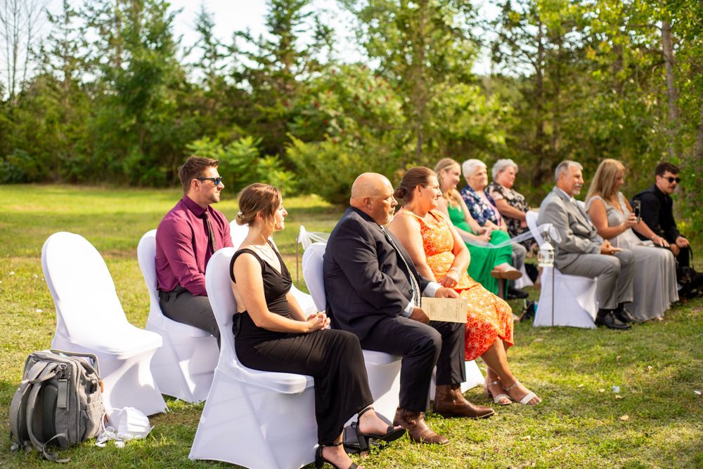 Guests seated in white chairs on a lawn for an outdoor wedding ceremony.