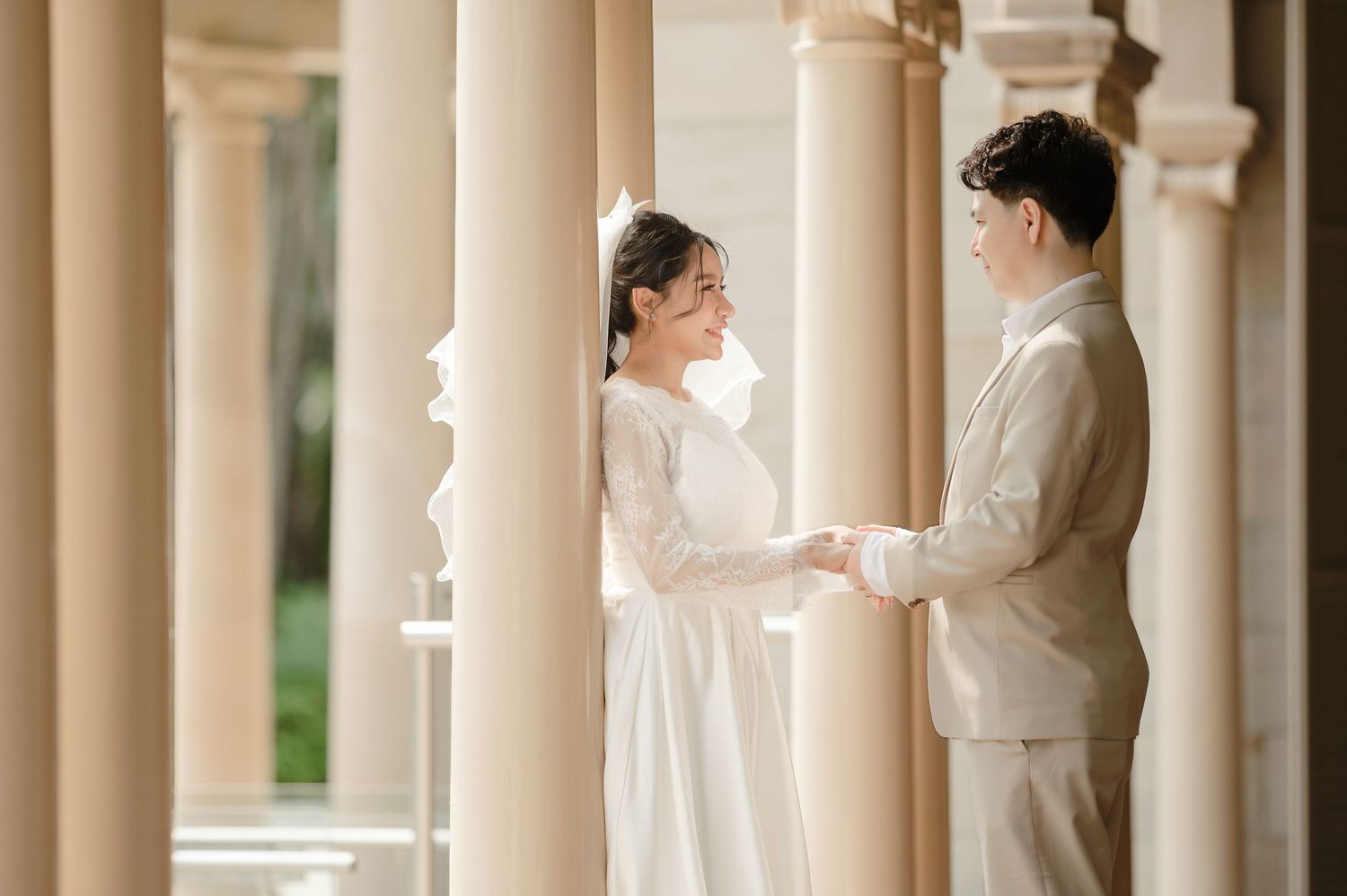 Couple in elegant wedding attire standing between classical columns.