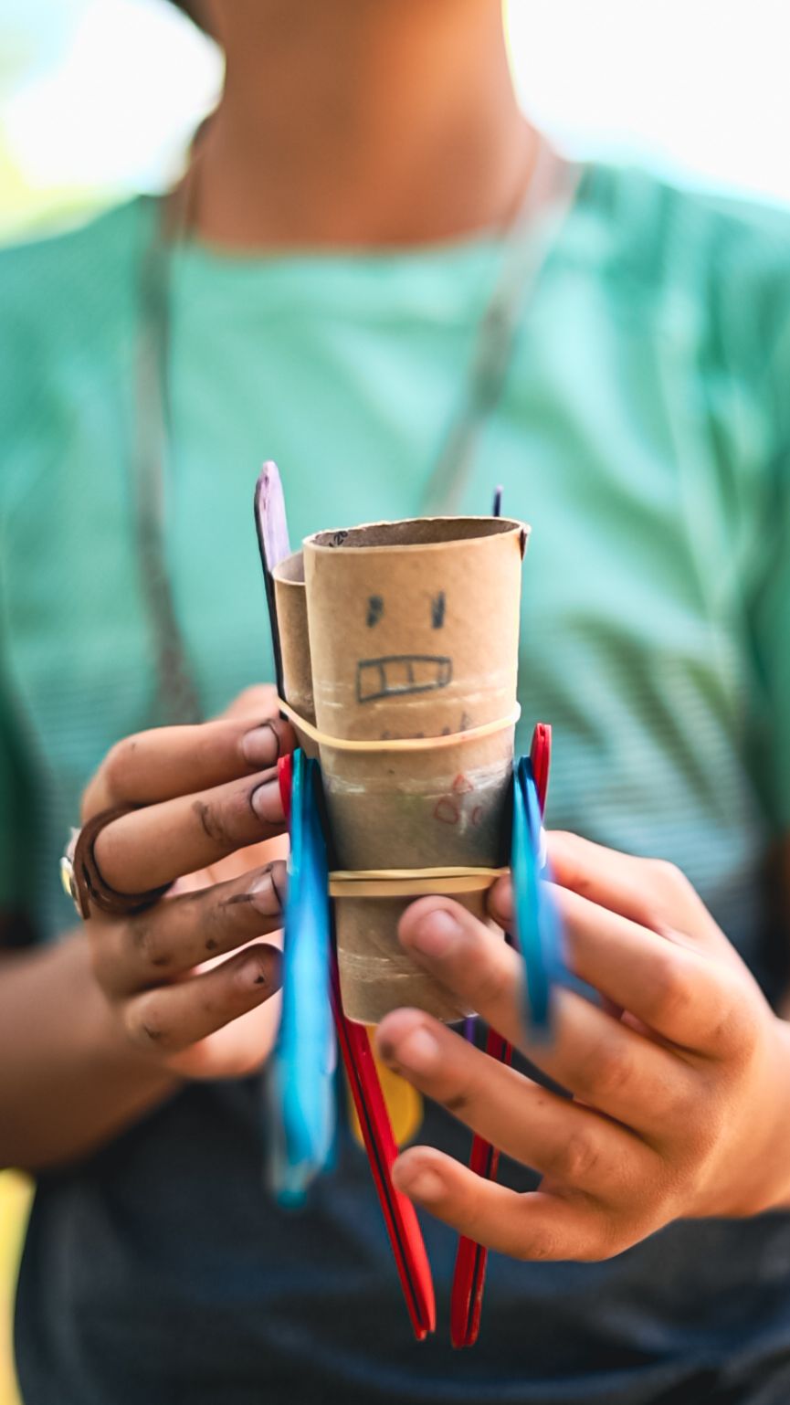 Handmade puppet crafted from toilet paper roll with drawn face and colorful pipe cleaner arms.