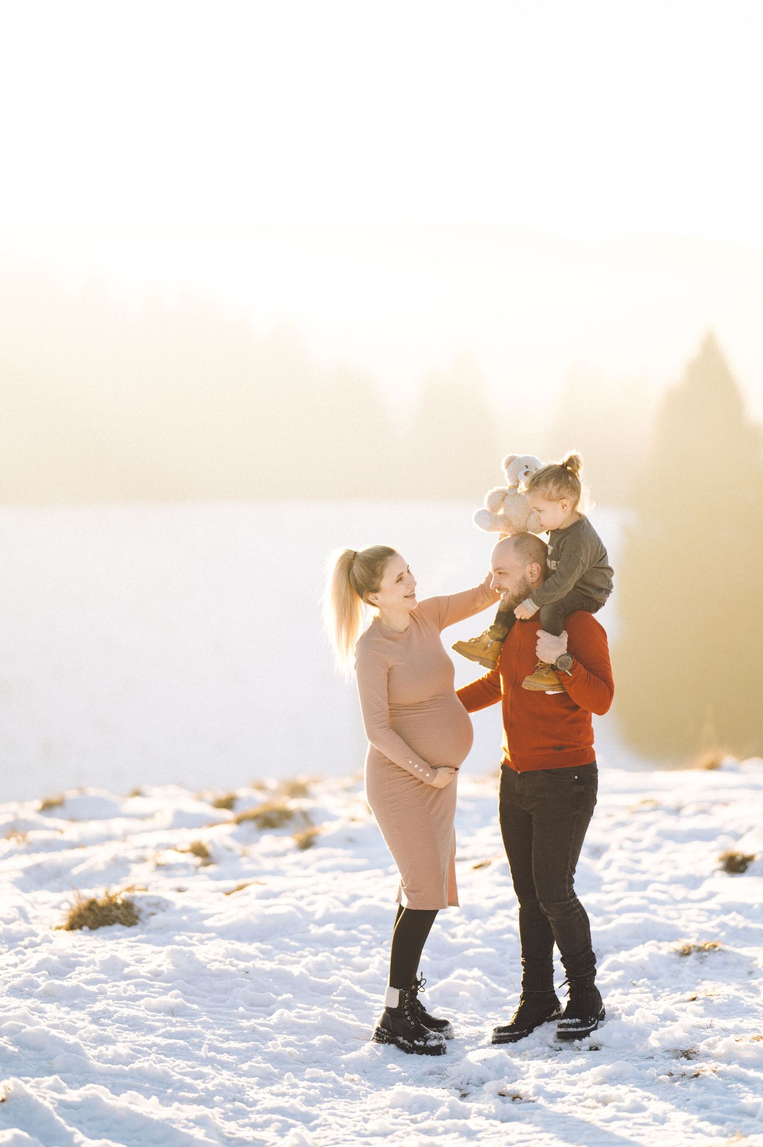 A family poses together in bright winter sunlight on snow-covered ground.