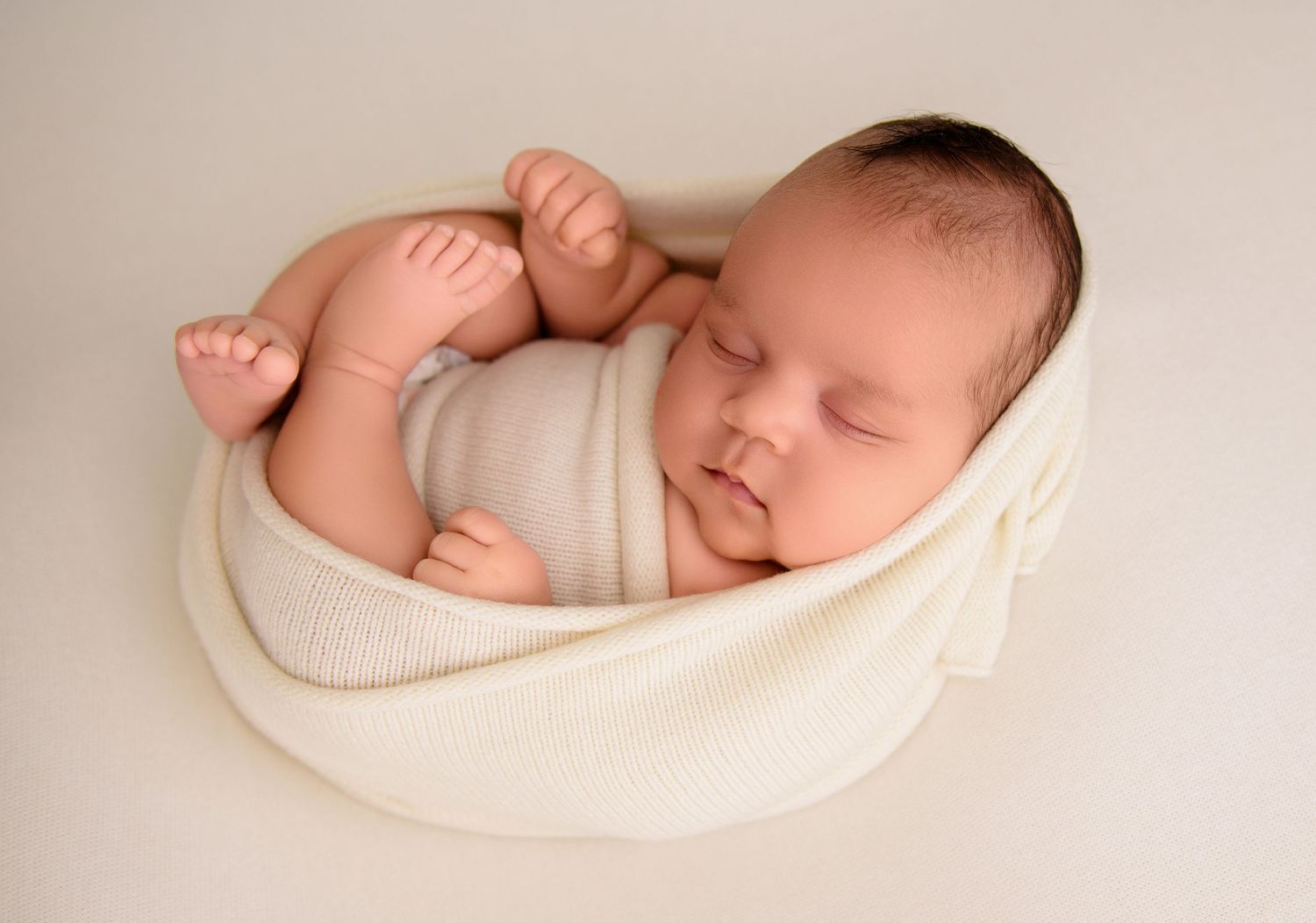 Peaceful newborn baby sleeping on soft white blanket in natural light.