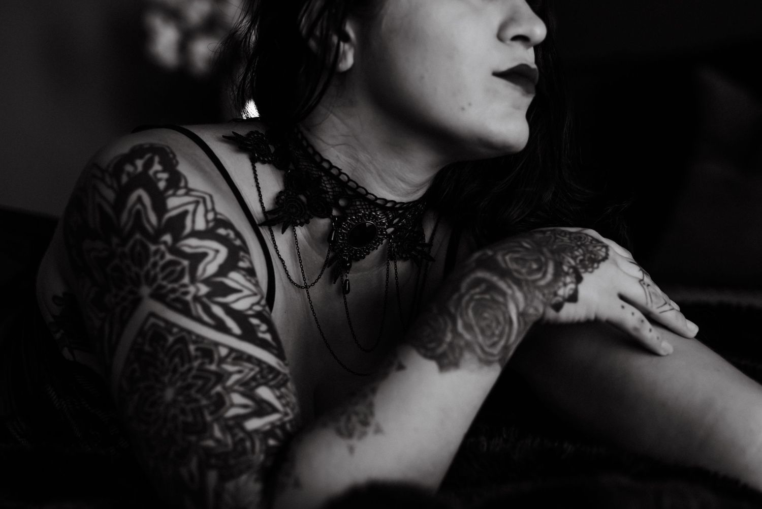 Artistic black and white photo showing detailed arm tattoos and mesh clothing in dramatic lighting.
