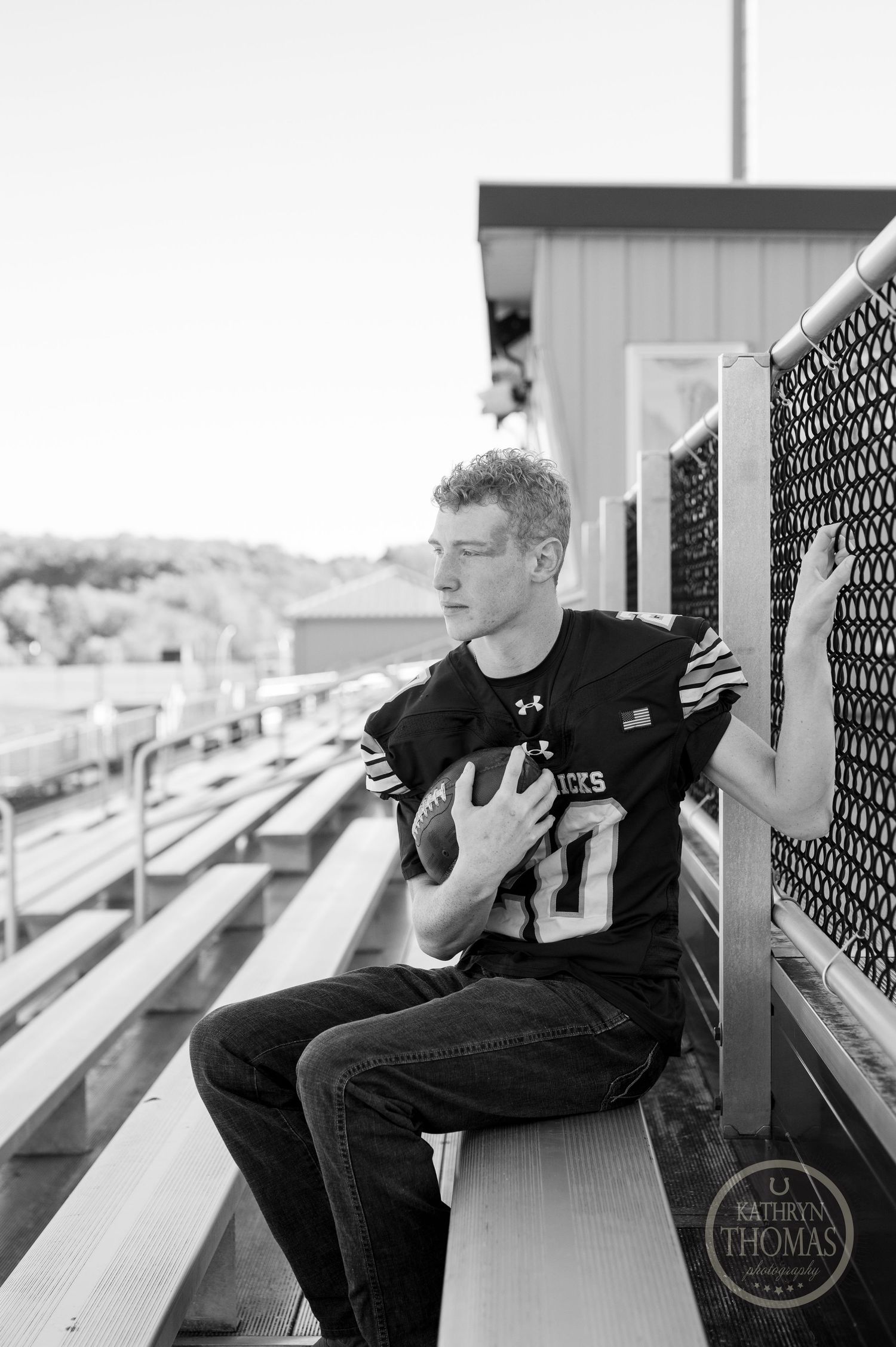 Black and white portrait of athlete in jersey posing on stadium bleachers.