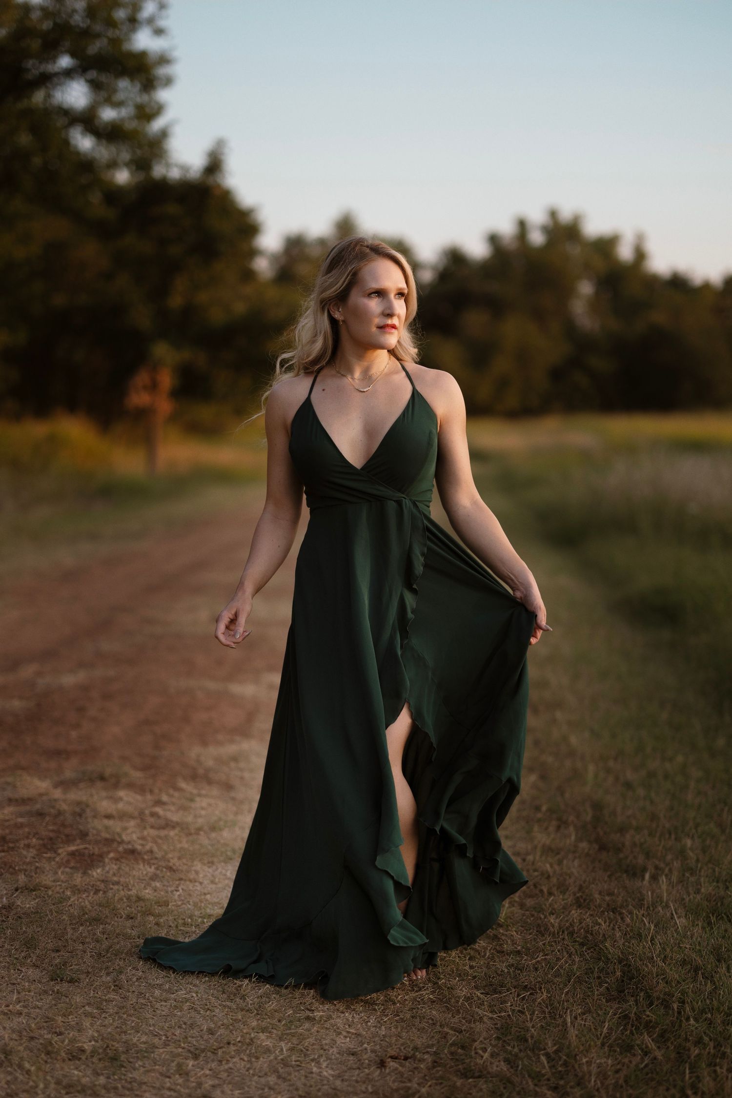 A forest path at sunset with someone wearing a flowing emerald green formal dress in motion.