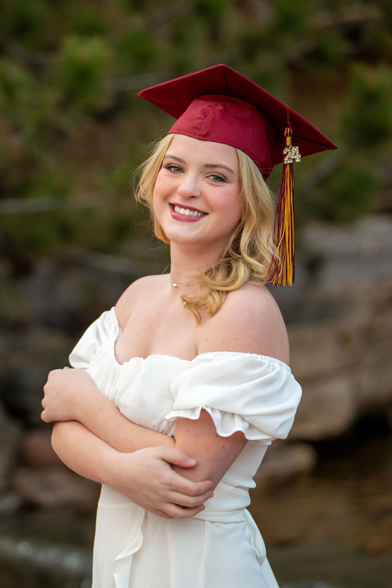 Graduate in white dress and red cap poses outdoors for graduation photos.
