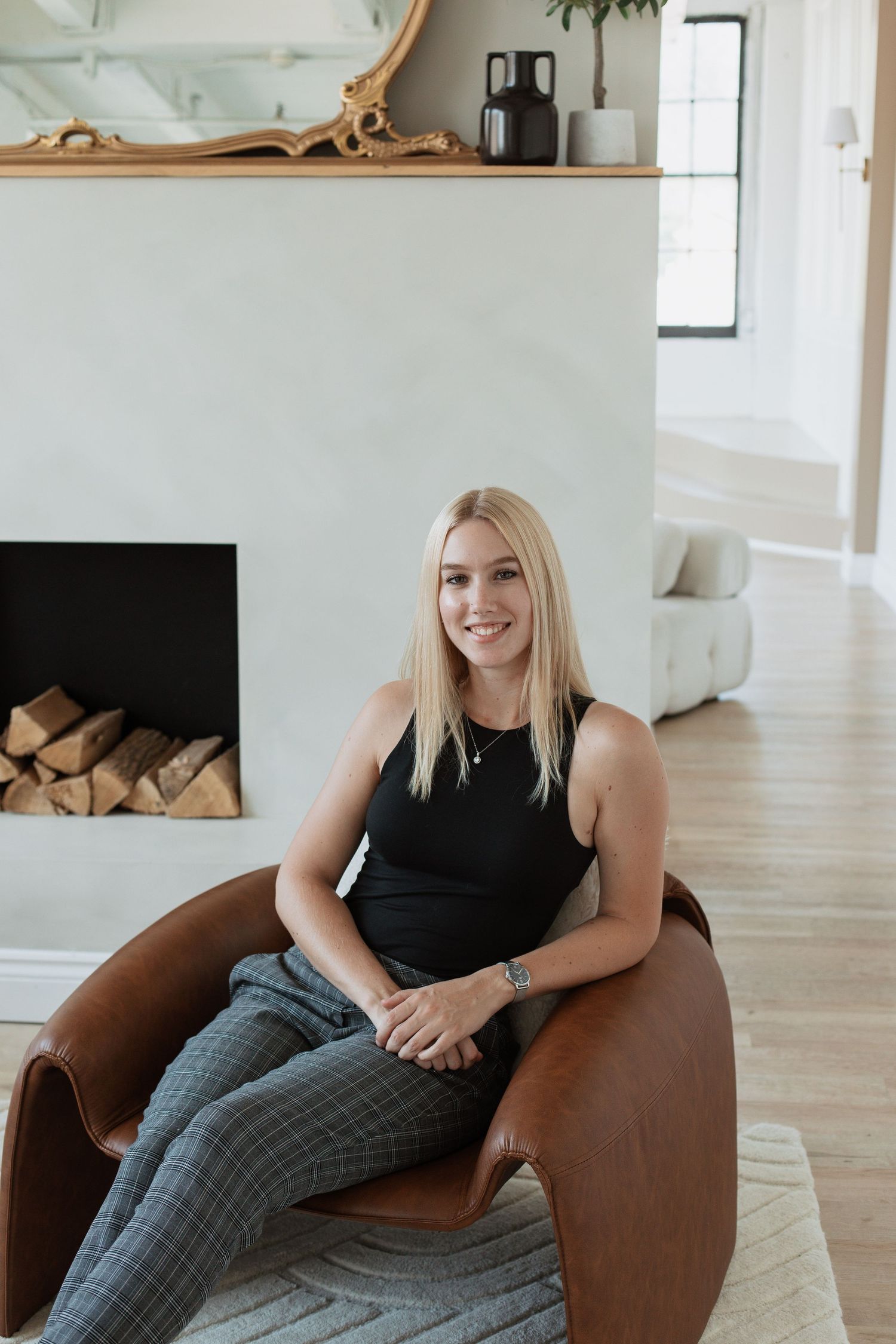 Modern interior with woman posing in brown leather chair next to decorative fireplace.