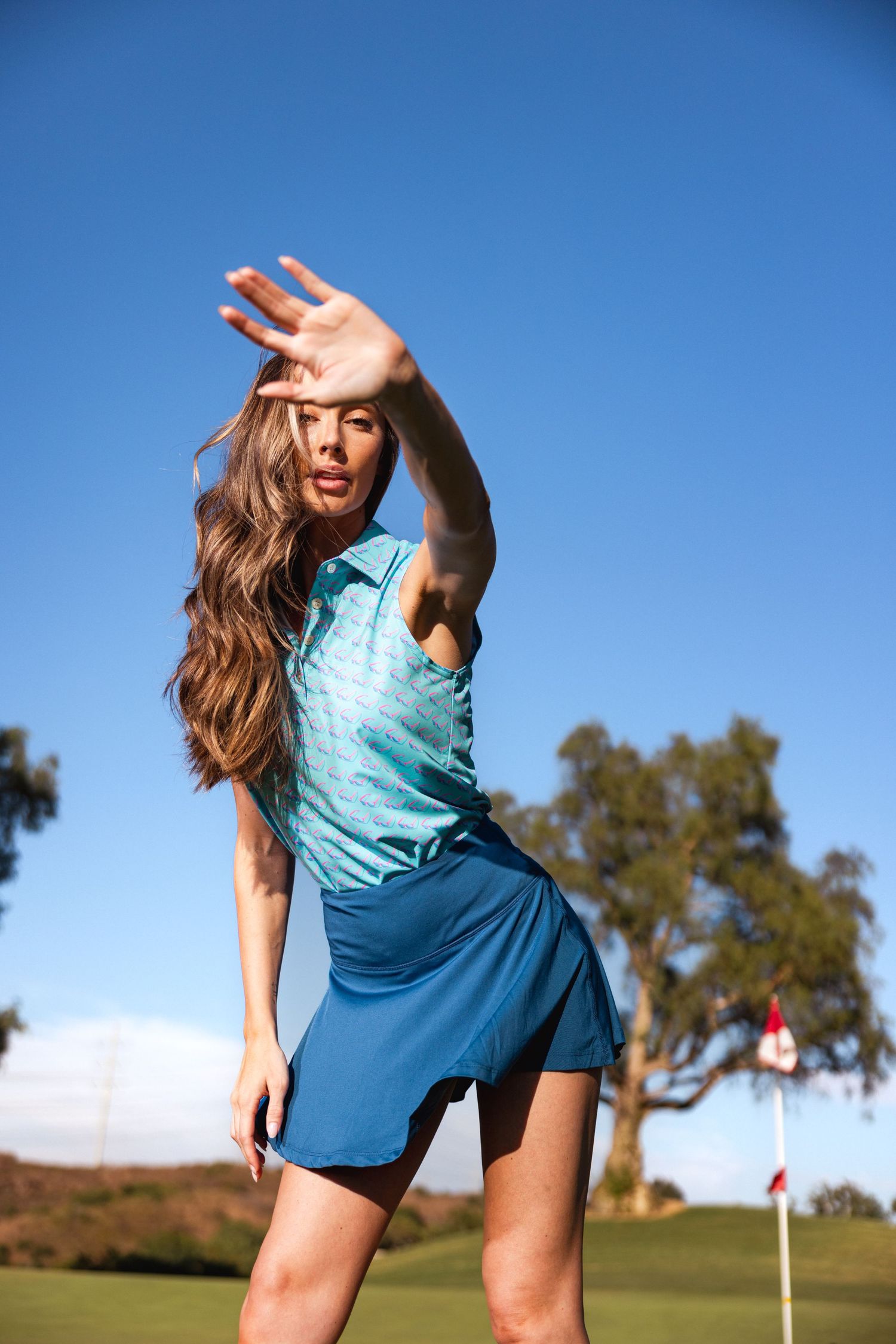 Golfer in blue athletic wear poses dynamically against bright blue sky on golf course.