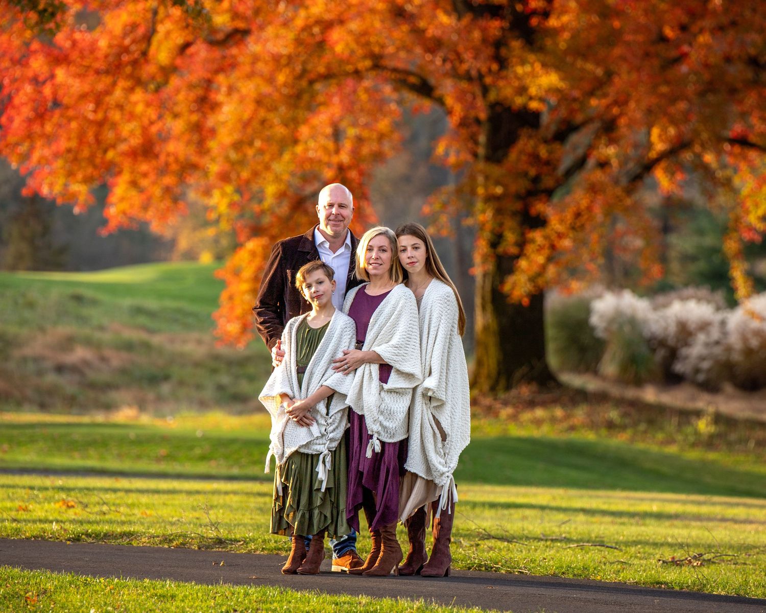 Five children sit together on a blue blanket in a grassy field on a fall day.