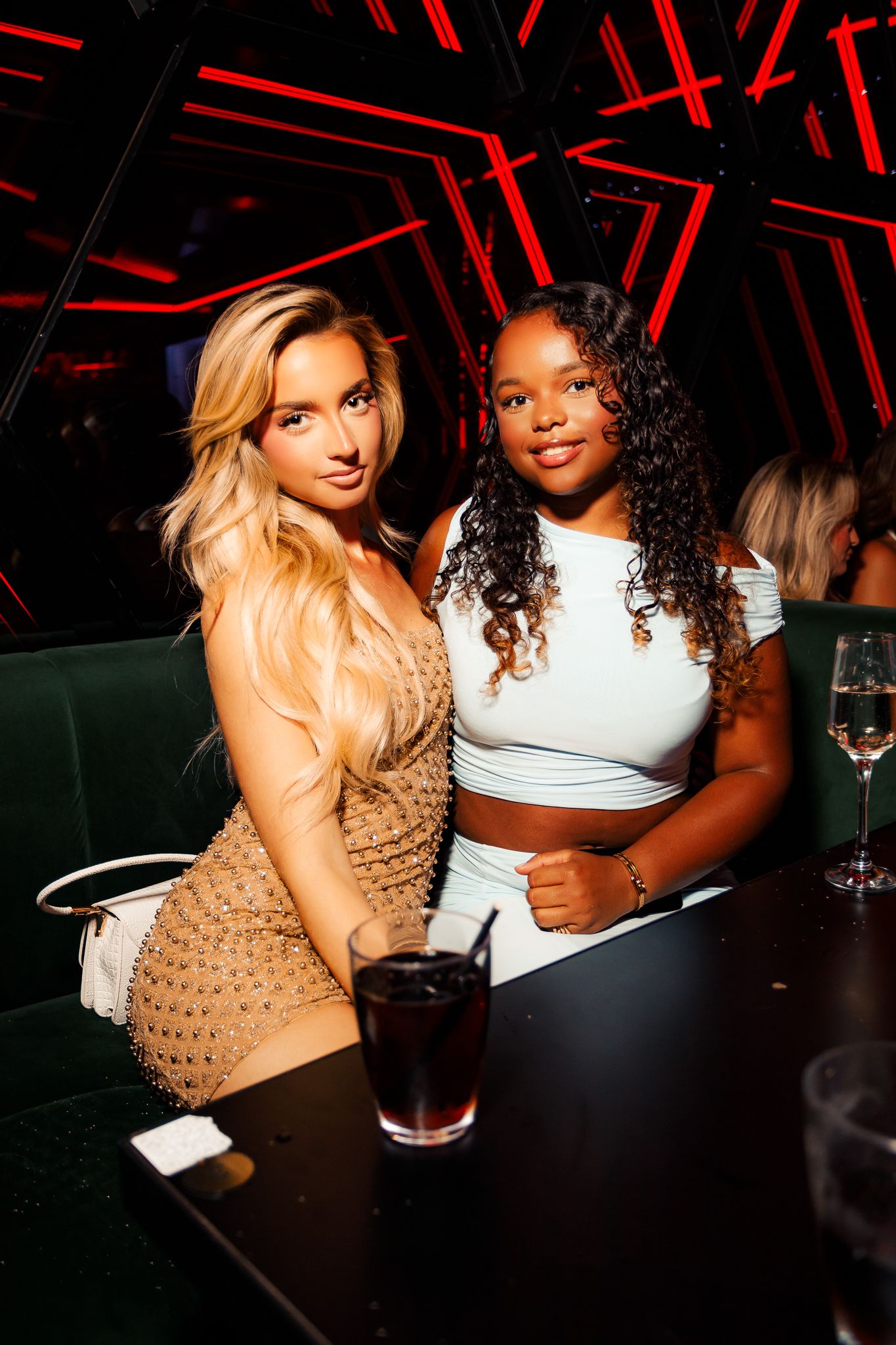 Two friends enjoying drinks together at a nightclub with red geometric lighting patterns on the walls.