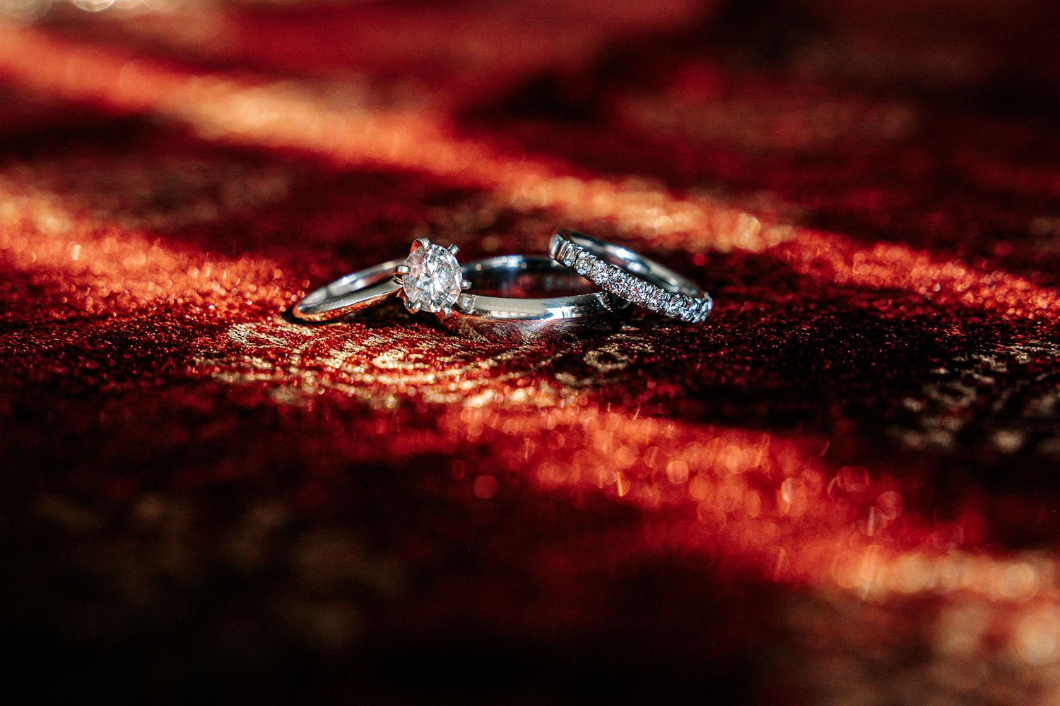 Wedding rings displayed on rich red velvet fabric with dramatic lighting.