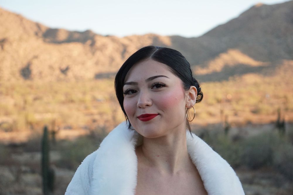 Woman in white fur collar posing against desert mountain backdrop.