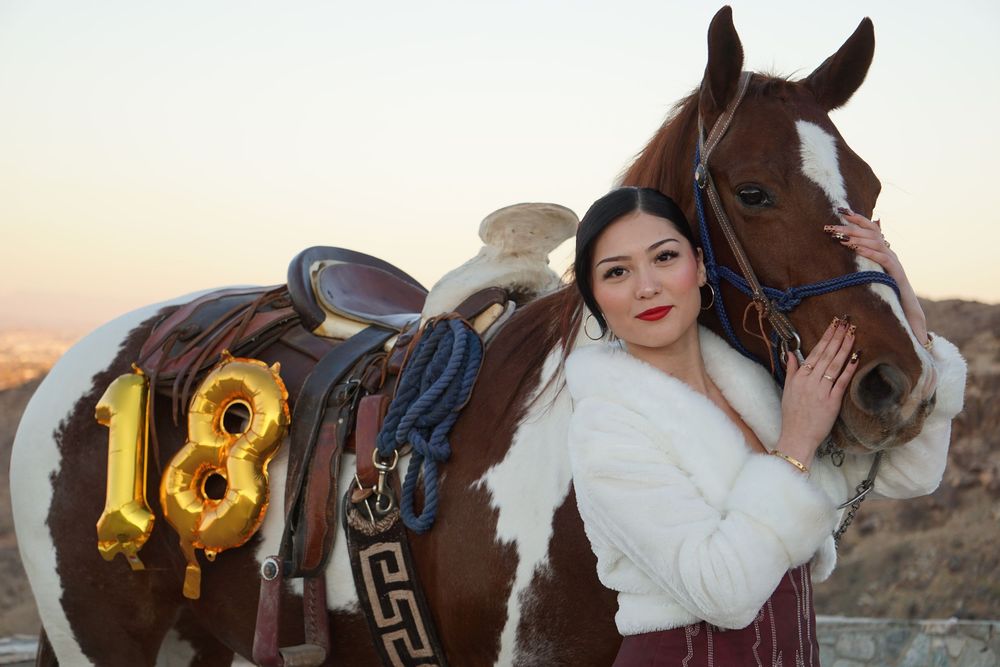 A couple in western attire poses with horses during a golden sunset photoshoot in the desert.