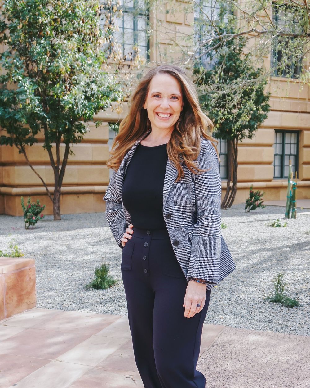 Professional business attire featuring a fitted black jumpsuit paired with a gray plaid blazer in an outdoor setting.
