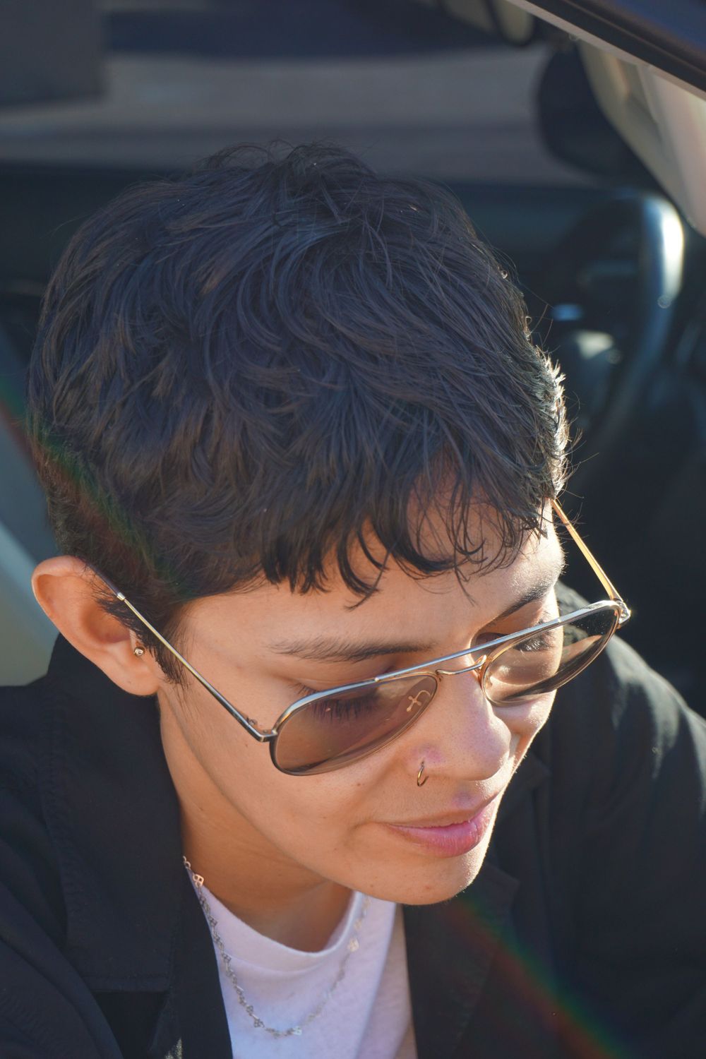 Person with curly hair and glasses smiling while sitting in car.