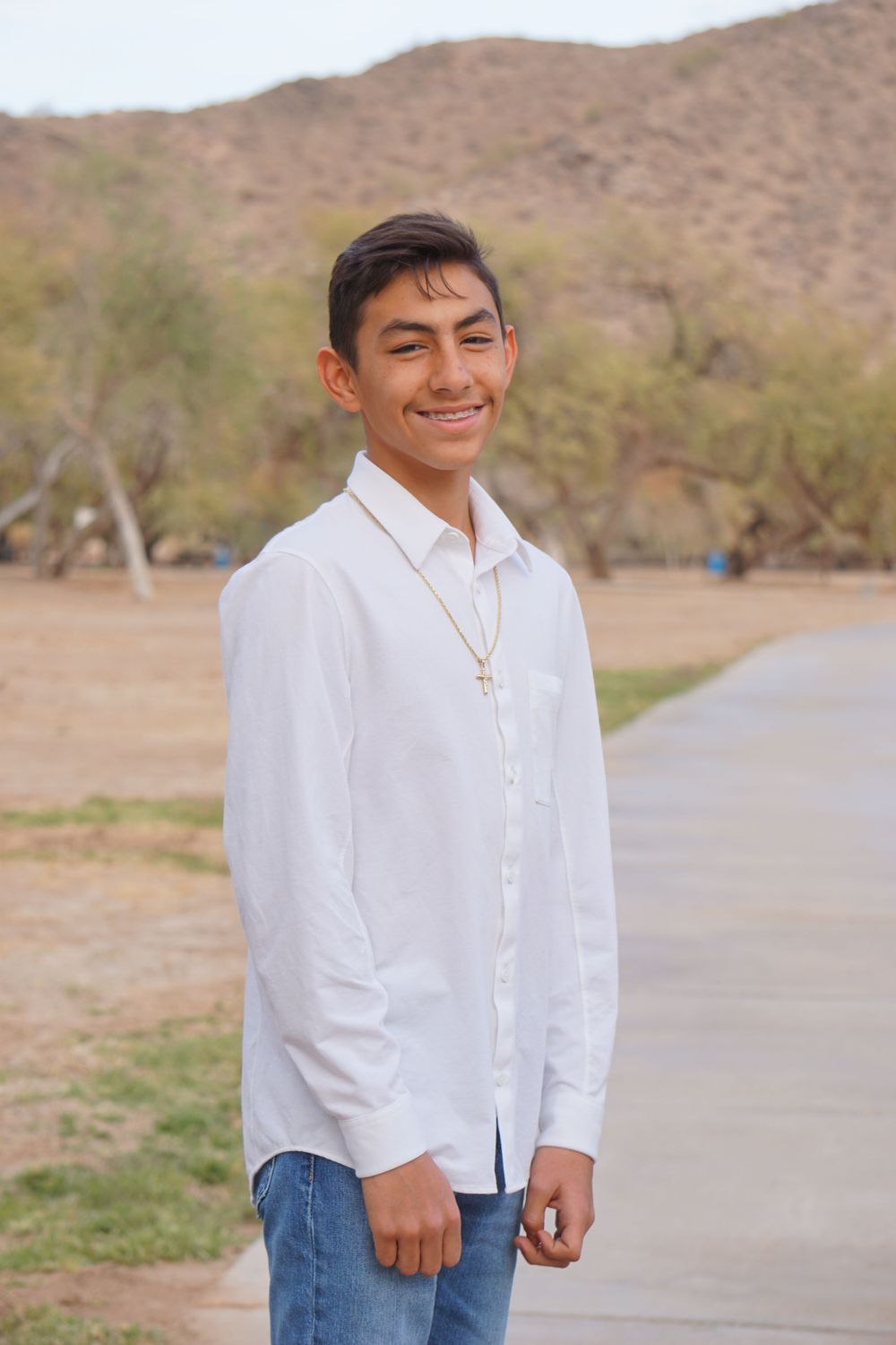 A person in a white button-down shirt and jeans stands against a desert mountain backdrop.
