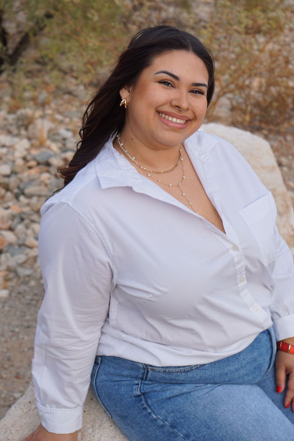 A person in a classic white shirt and jeans poses outdoors against a rocky background.