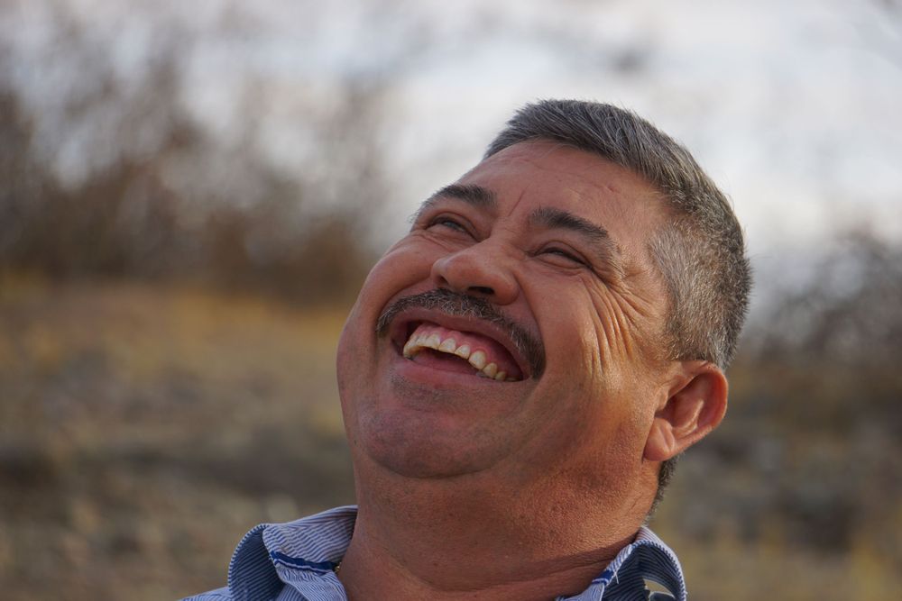 Two people smile warmly while posing together in an outdoor desert setting.