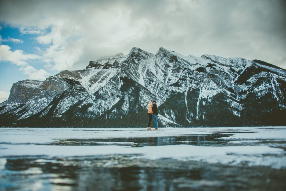 Winter scene with snowy Mount Cascade rising behind a solitary figure at frozen Lake Minnewanka in Banff National Park.