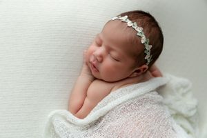 A peaceful newborn sleeps on a white blanket while wearing a delicate floral headband.