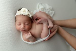 Newborn baby sleeping peacefully on white backdrop while wearing delicate floral headband during professional photo session.
