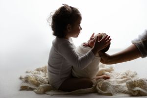 A silhouetted figure holding hands with an adult in a gentle backlit scene against a white background.