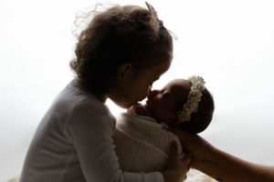 A silhouetted figure tenderly embracing and kissing a baby against a bright white background.