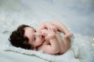 Sweet baby lying on soft white blanket against cloudy gray backdrop during professional photo session.