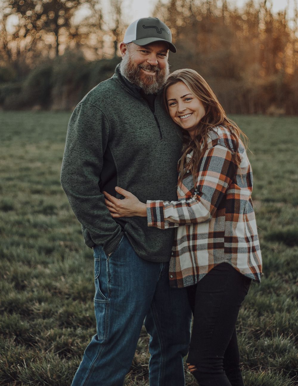 Smiling couple embracing in green field during warm golden sunset light.