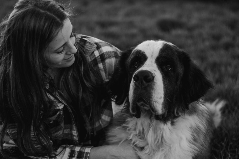Woman in plaid shirt leaning close to Saint Bernard dog face in black and white photo.