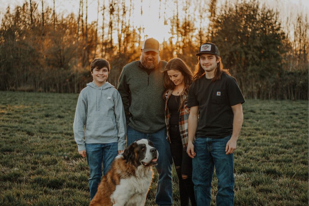 Smiling family with Saint Bernard dog enjoying a warm sunset in an open field.