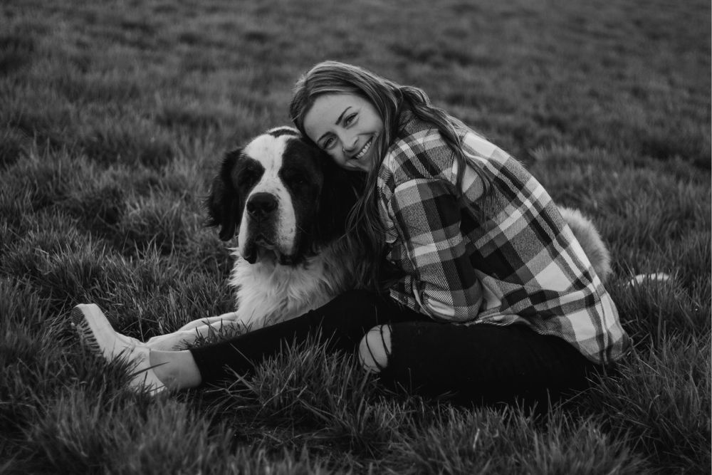 Woman in plaid shirt cuddling with Saint Bernard dog on grass in black and white.