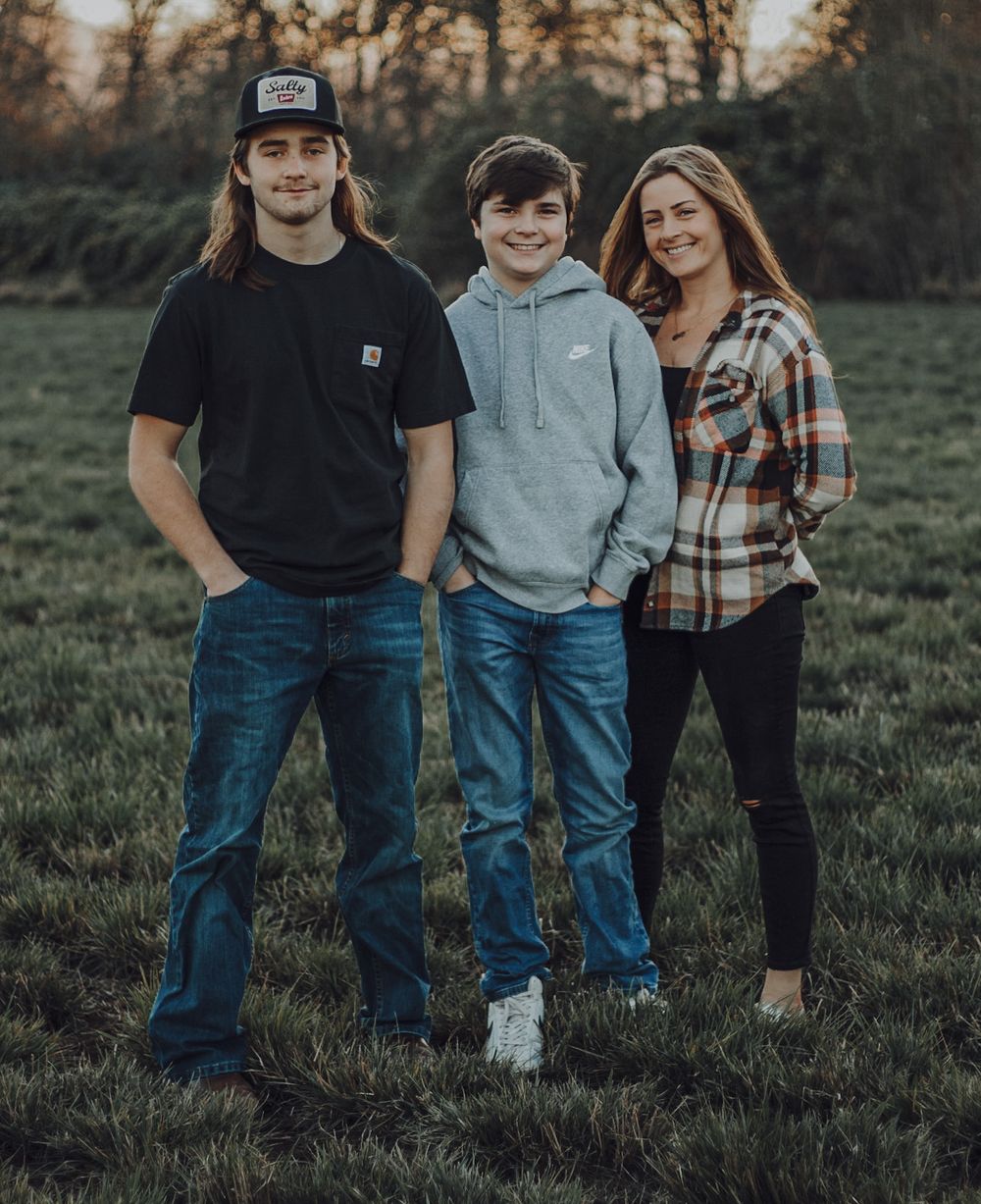 Two teenage boys and a woman posing together in green field at dusk.