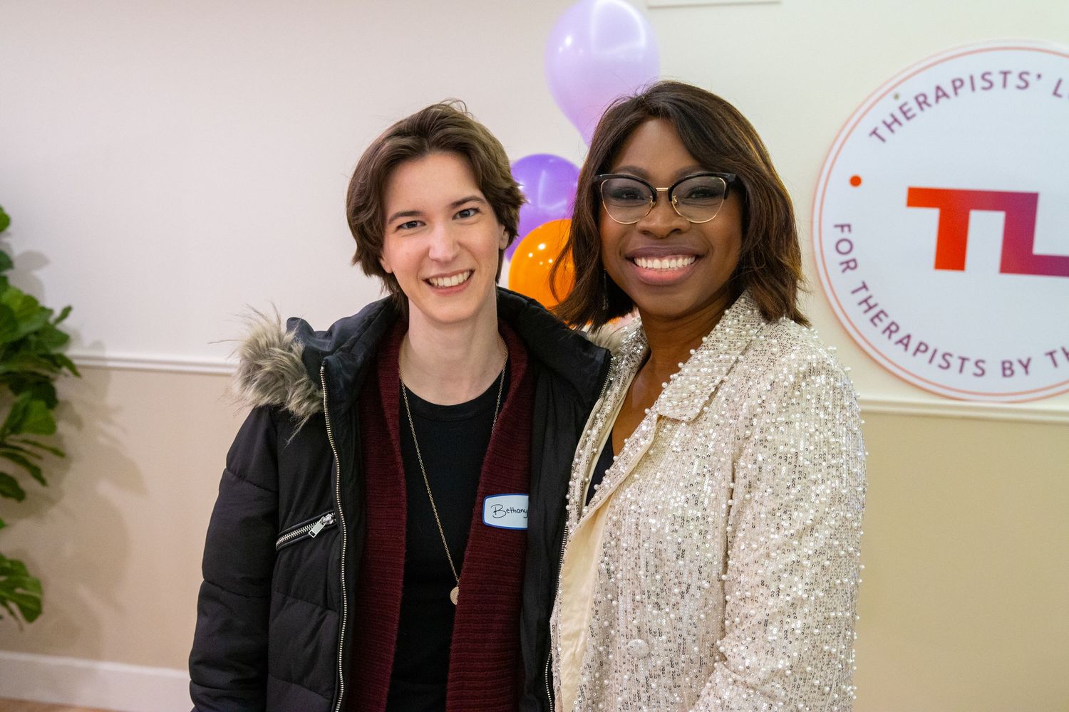 Two people stand together smiling at a professional event with a TL logo visible on the wall behind them.