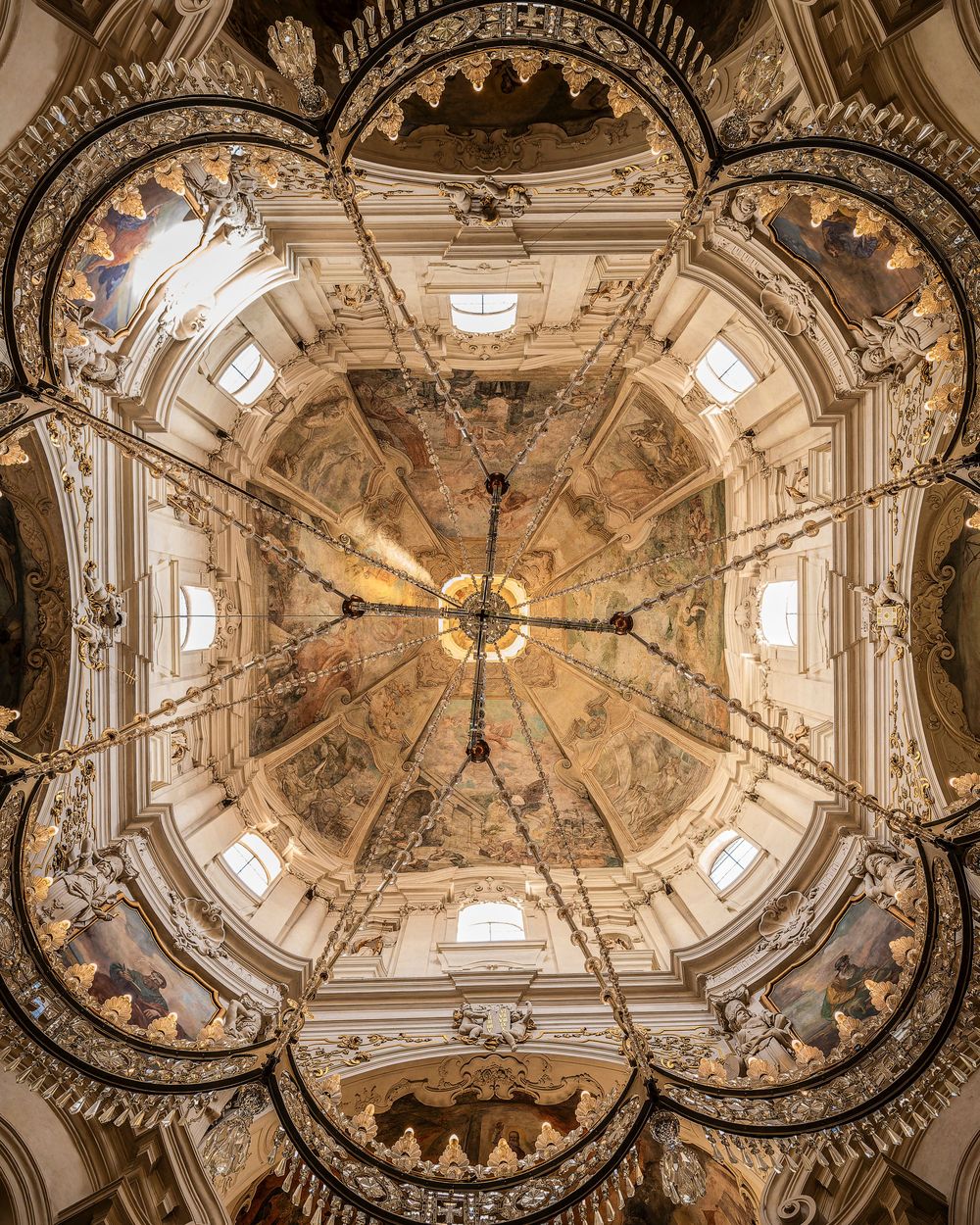 Ornate baroque ceiling fresco inside a cathedral with intricate architectural details and natural light streaming through windows.