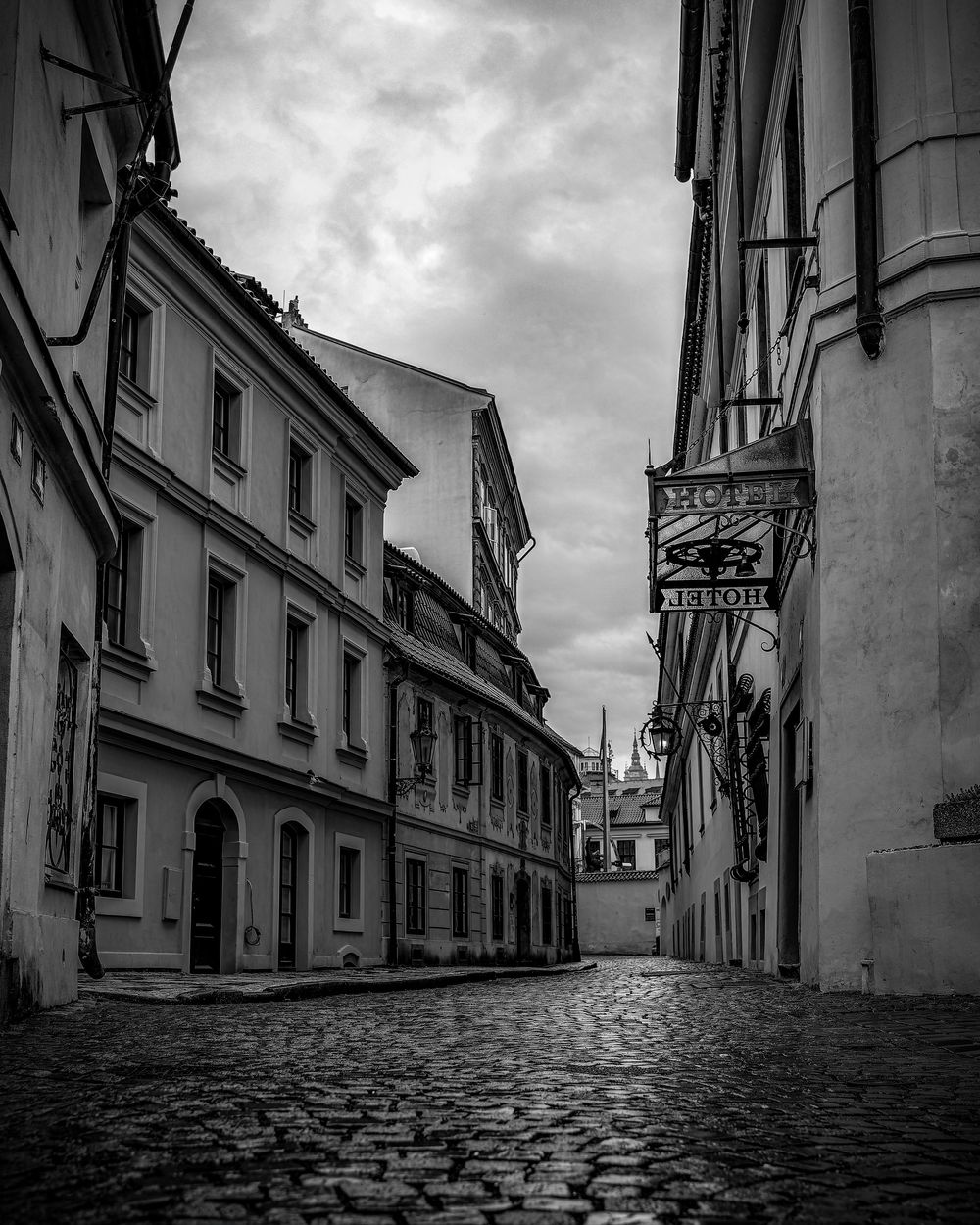 A dramatic black and white panoramic view of empty cobblestone streets and historic buildings in Prague's old town.